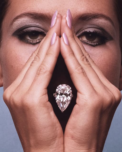 A pear-shaped diamond ring held between two hands, eyes above